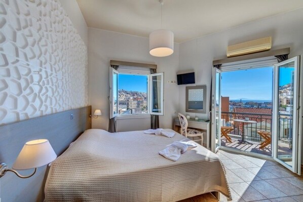 Een hotelkamer met een bed, een bureau, een stoel, een televisie en een balkon met uitzicht op de stad.