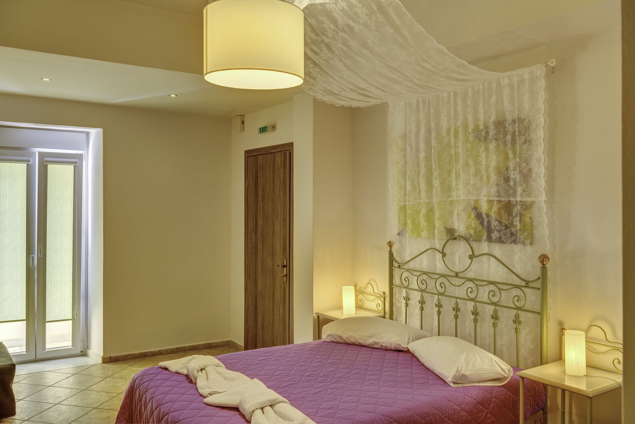 A bedroom with a bed, a nightstand, a lamp, a door, and a window.