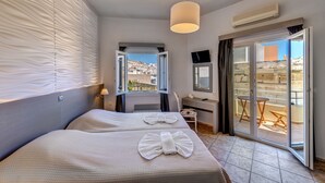 Habitación de hotel con dos camas, un escritorio, una silla, un televisor y un ventanal corredero a un área exterior.