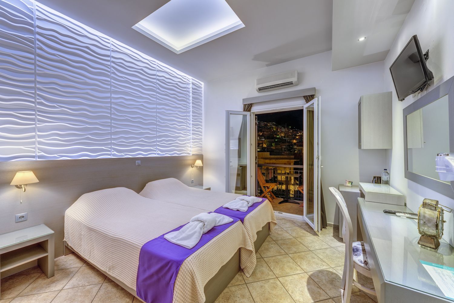 A modern hotel room with a large bed, a desk with a mirror, and a balcony with a city view.