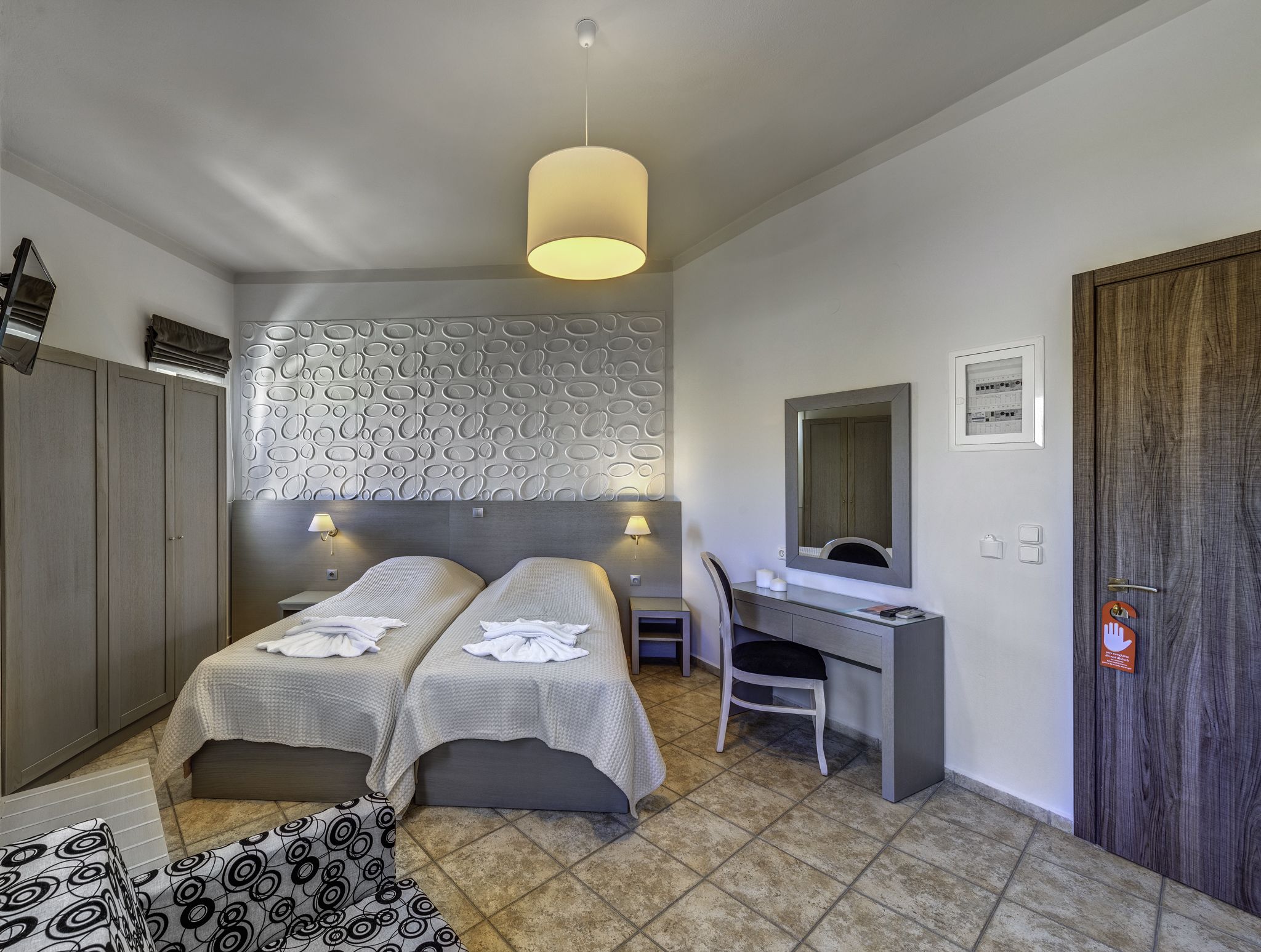 A hotel room with two beds, a desk, a chair, a wardrobe, and a bathroom door.
