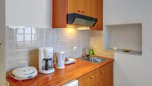 Una cocina compacta con armarios de madera, un lavamanos de acero inoxidable, una cafetera y un hervidor.