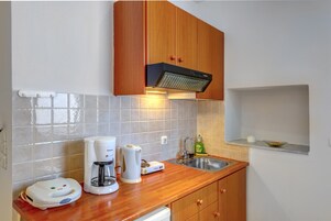 Una cocina compacta con armarios de madera, un lavamanos de acero inoxidable, una cafetera y un hervidor.