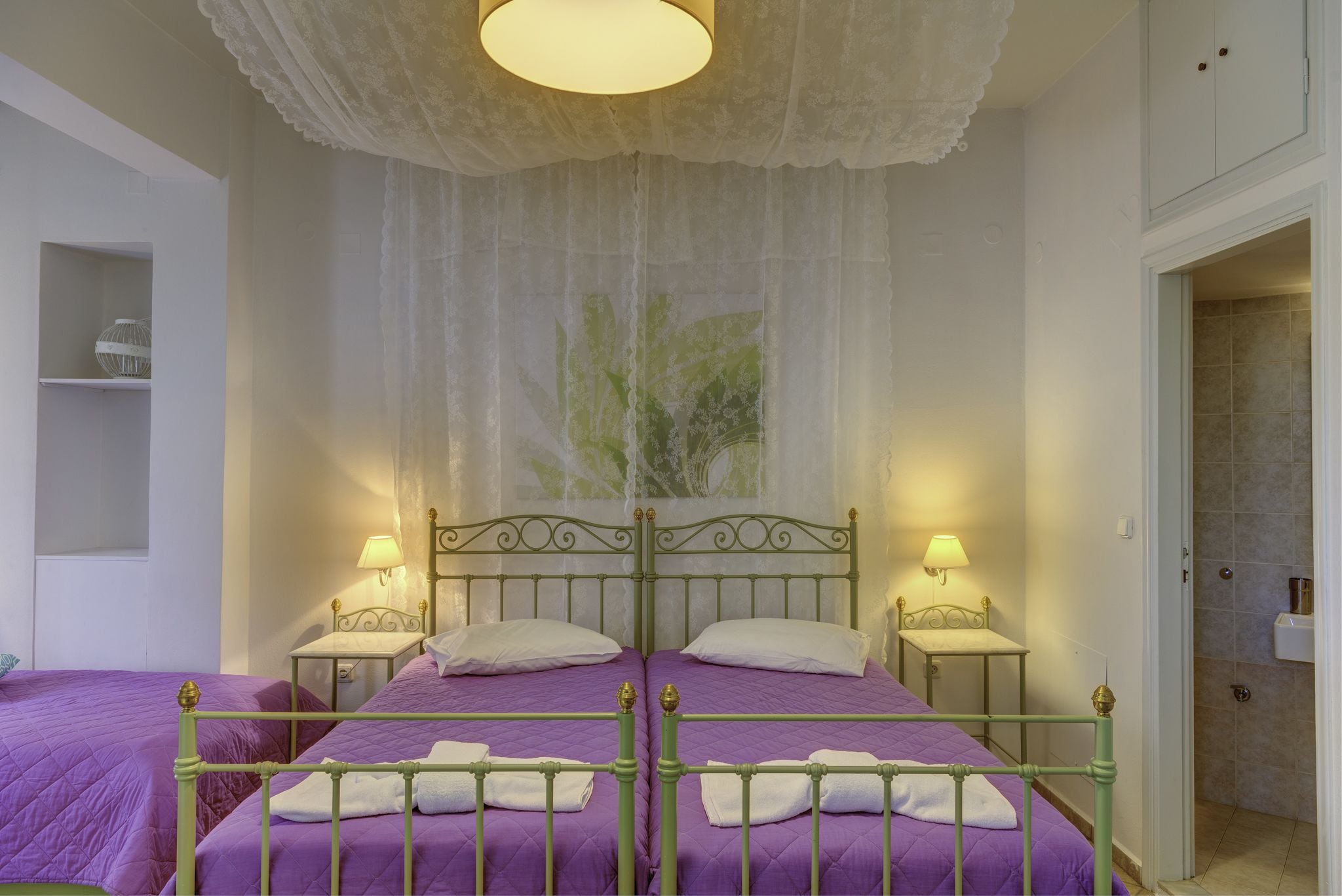 A room with a bed, two bedside tables, a shelf, and a door leading to a bathroom.
