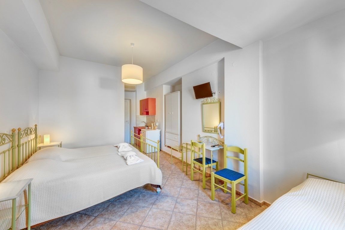 Una camera d'albergo con due letti, una scrivania, una sedia, uno specchio e un bagno sullo sfondo.