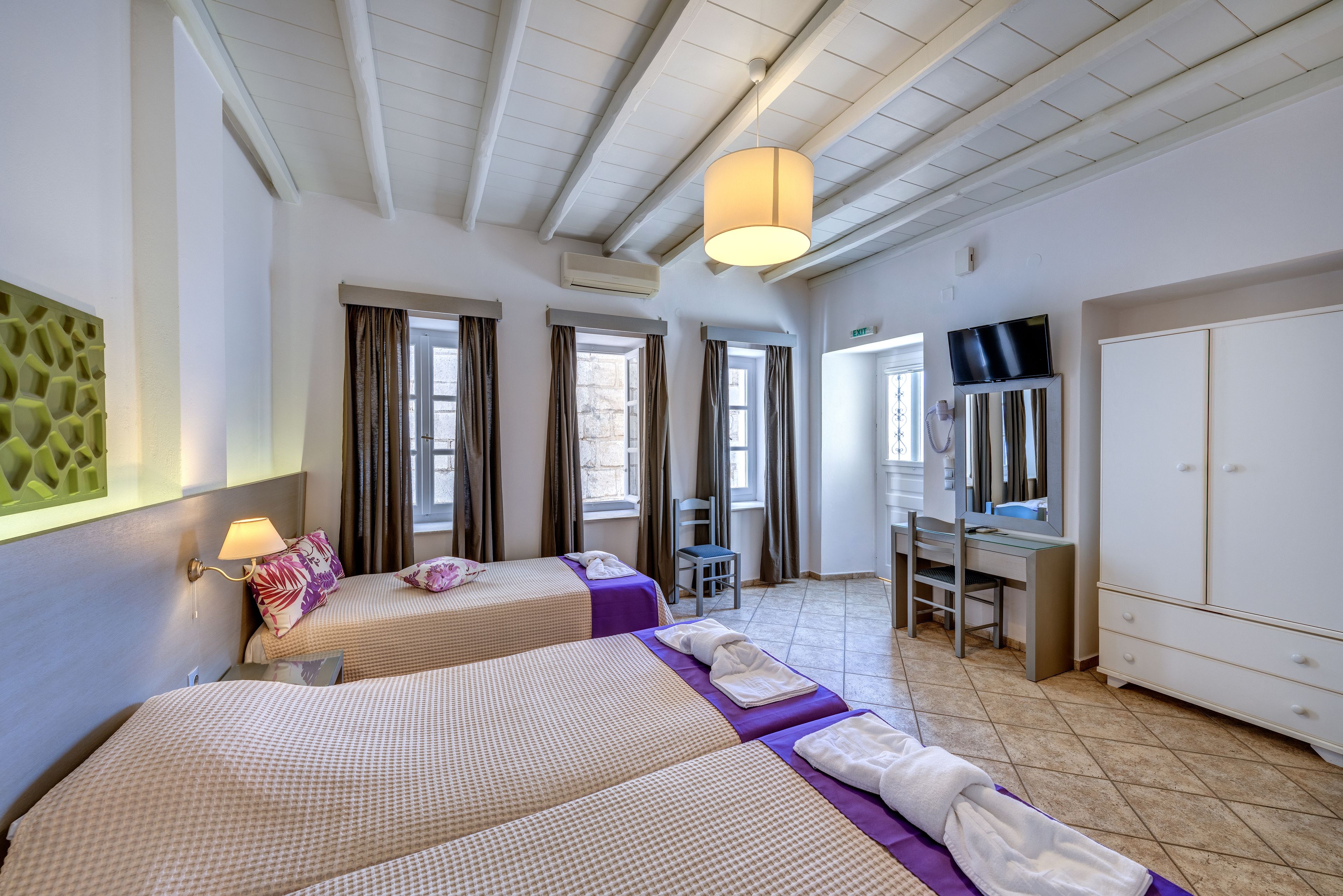 A hotel room with two beds, a desk, a chair, a TV, and a wardrobe.