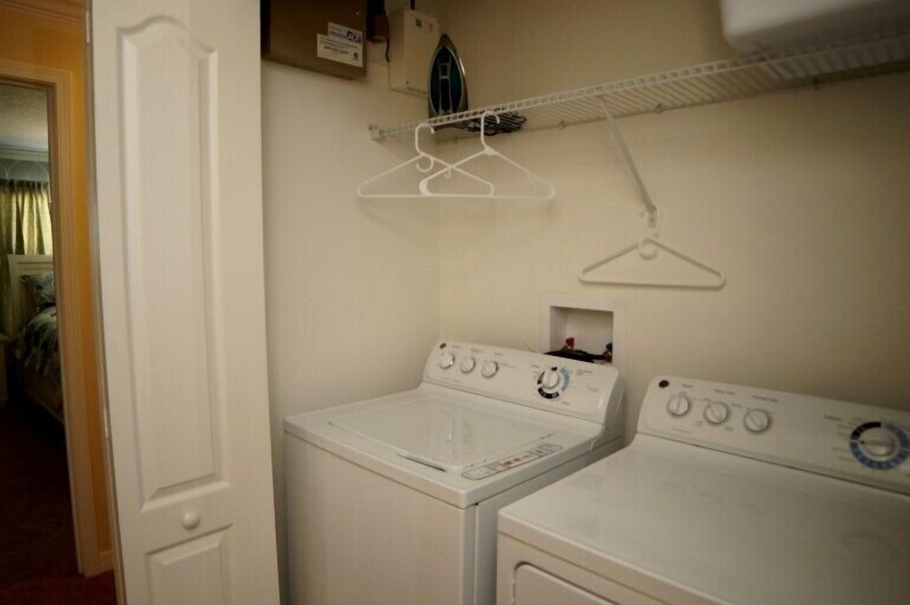 A laundry room with two white washers and dryers, a drying rack, and a small ironing board.