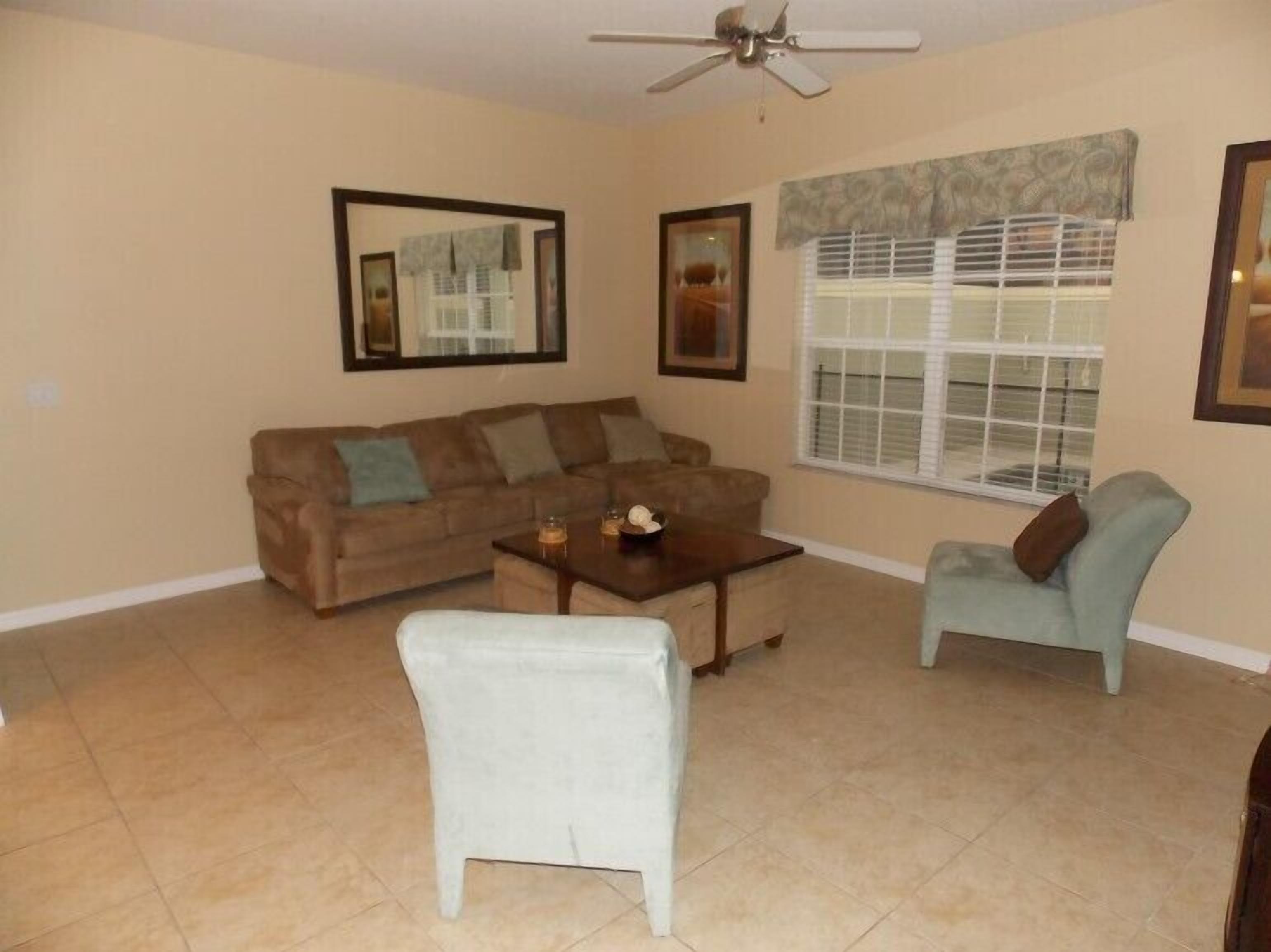 A living room with a brown sofa, a white armchair, a coffee table, and a window with blinds.