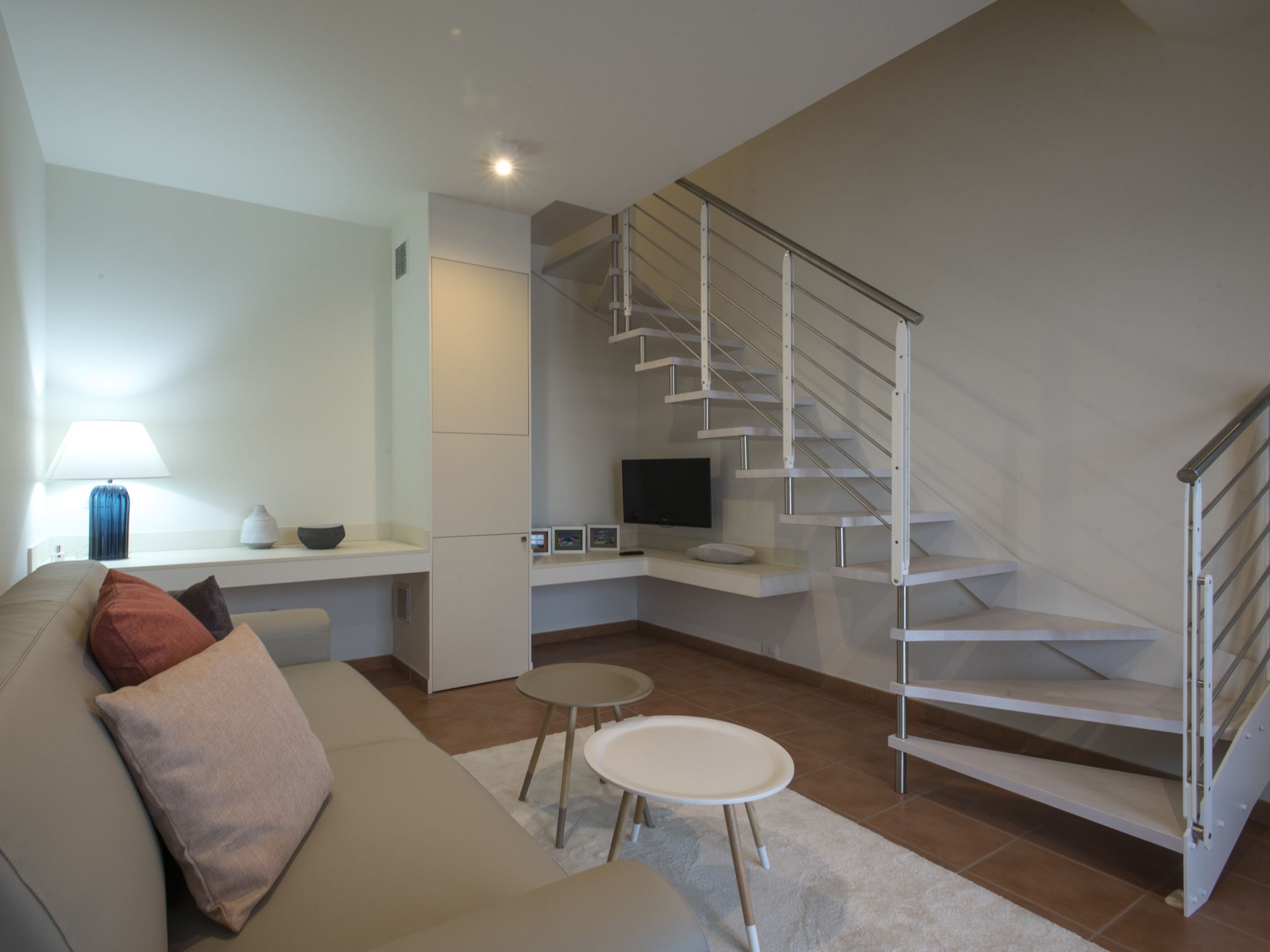 A modern living room with a staircase, a sofa, a coffee table, and a TV.