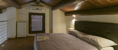 A bedroom with a wooden ceiling, a bed with a headboard, a radiator, and a door with blinds.