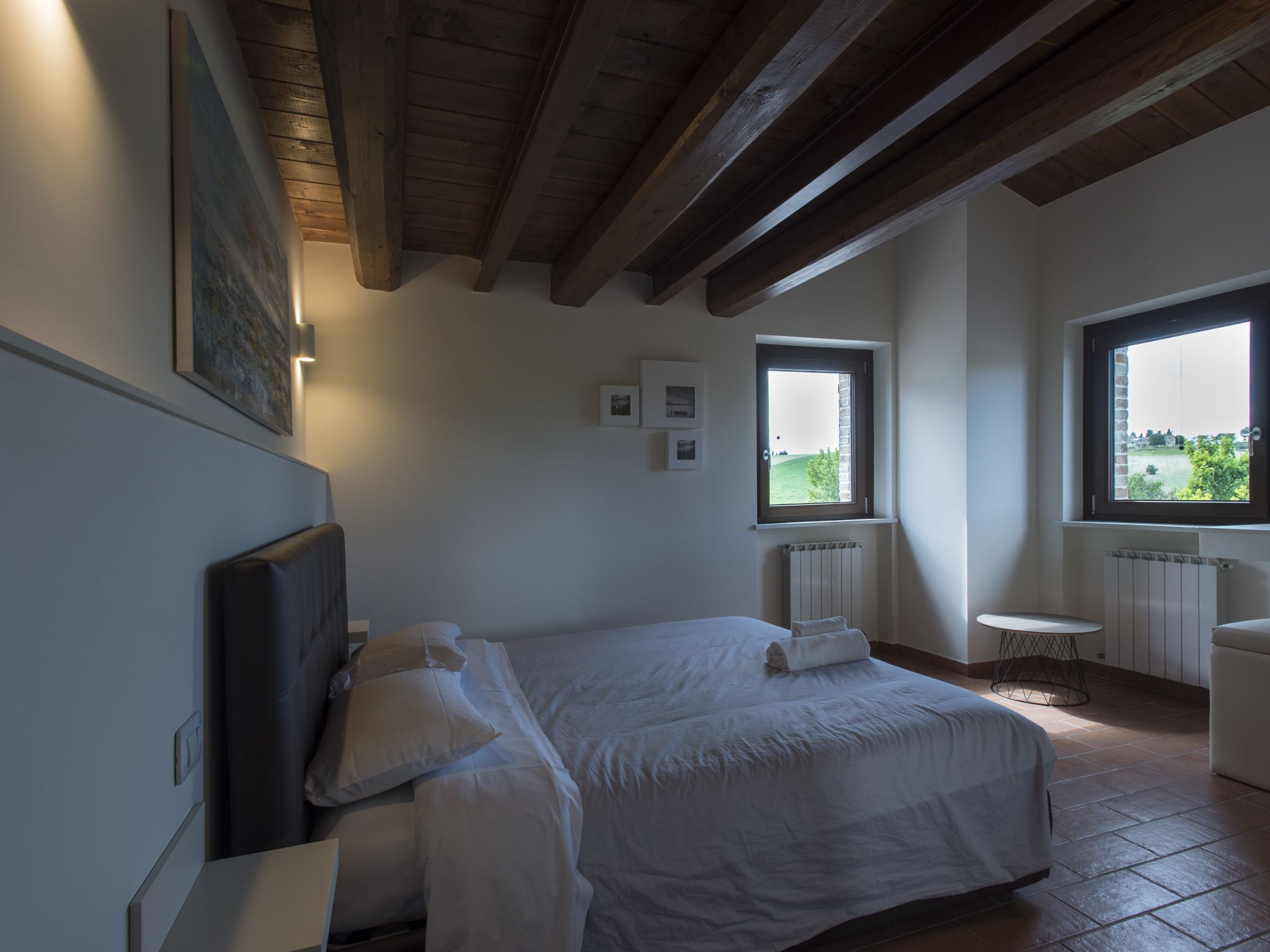 Una camera da letto con un letto grande, due finestre, un termosifone e un tavolino rotondo.