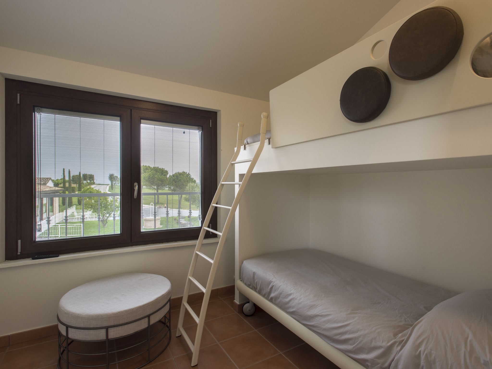 A bunk bed room with a window, a ladder, and a small round table.