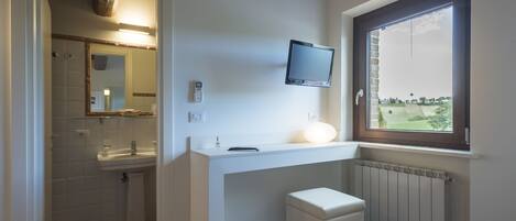 A modern bathroom with a white vanity, a small stool, a mirror, and a television mounted on the wall.