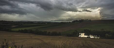 Paisaje rural con campos, un pequeño estanque y cielo nublado.