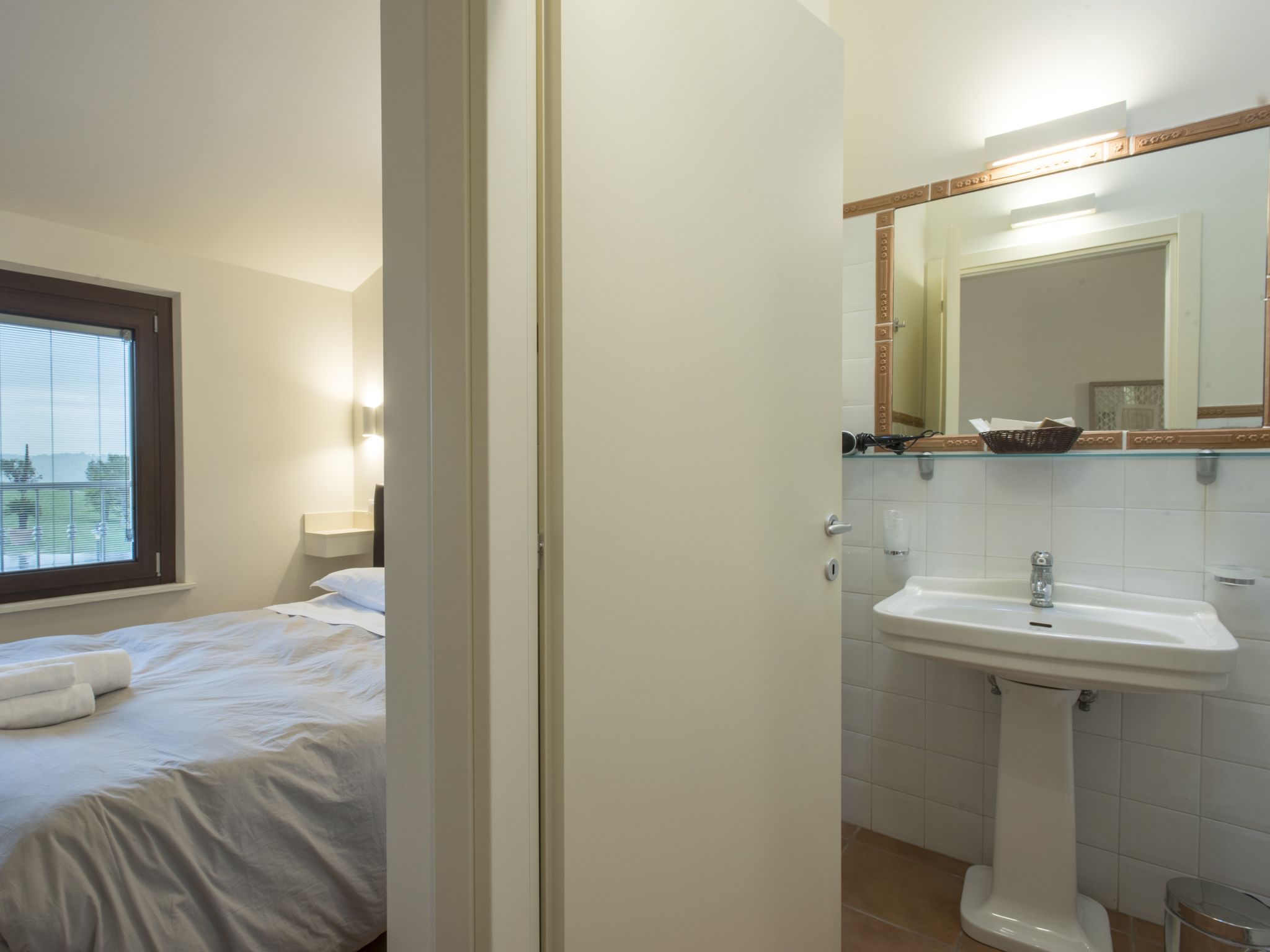 A hotel room with a bed, a window, a bathroom with a sink and mirror.