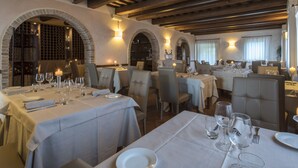 A restaurant with tables set for dining, featuring exposed wooden beams and arched brick walls. - Osteria dei Segreti (Appignano)
