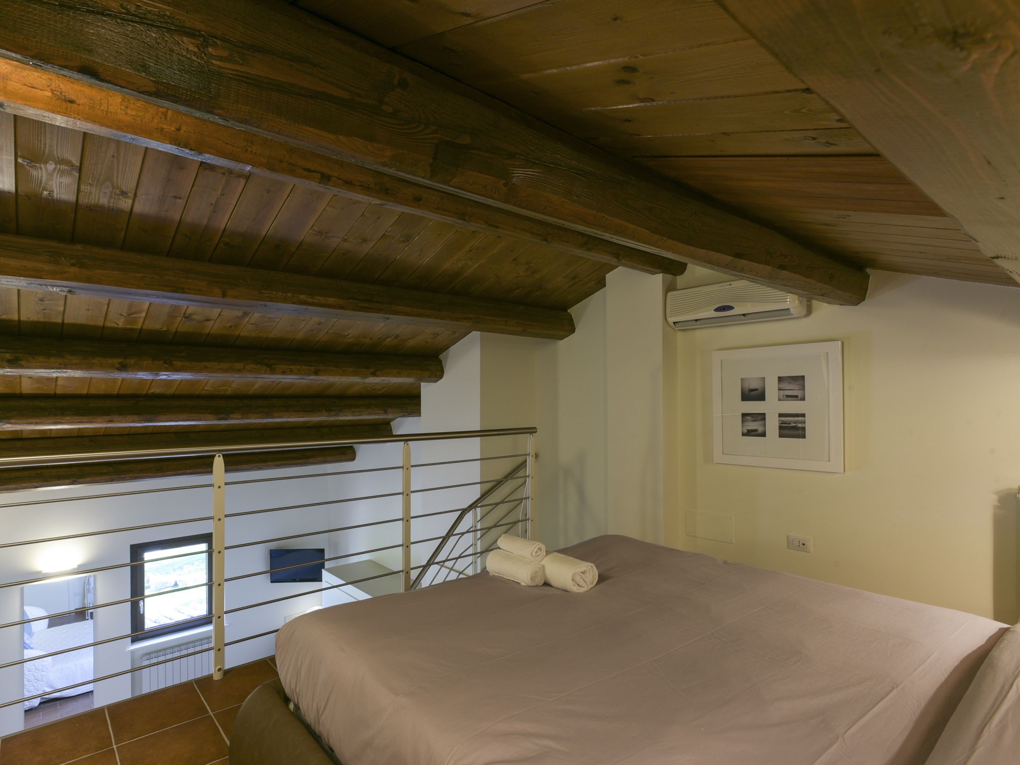 Un dormitorio con techo de madera, una cama con manta color beige, una ventana y un aire acondicionado instalado en la pared.