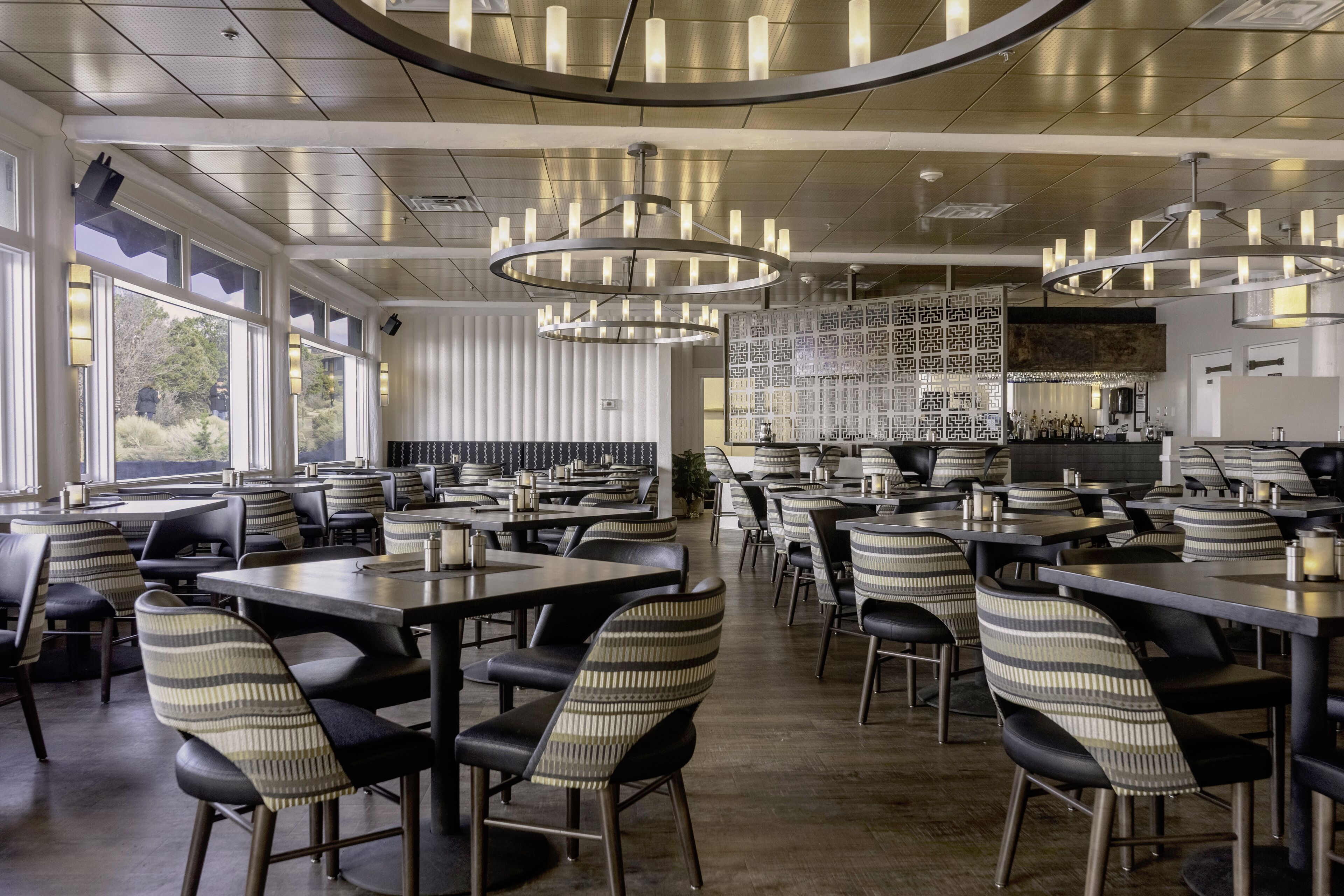 Un restaurante moderno con techos altos, candelabros circulares y sillas tapizadas a rayas.