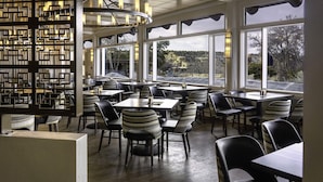 A restaurant with a modern interior, featuring a geometric wall design, multiple tables and chairs, and large windows offering views of the outdoors.