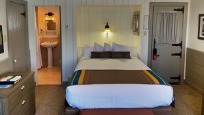 A hotel room with a bed, bedside table, and a bathroom visible through an open door.