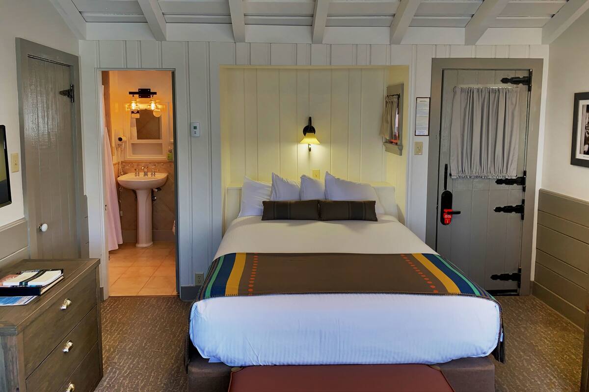 A hotel room with a bed, bedside table, and a bathroom visible through an open door.