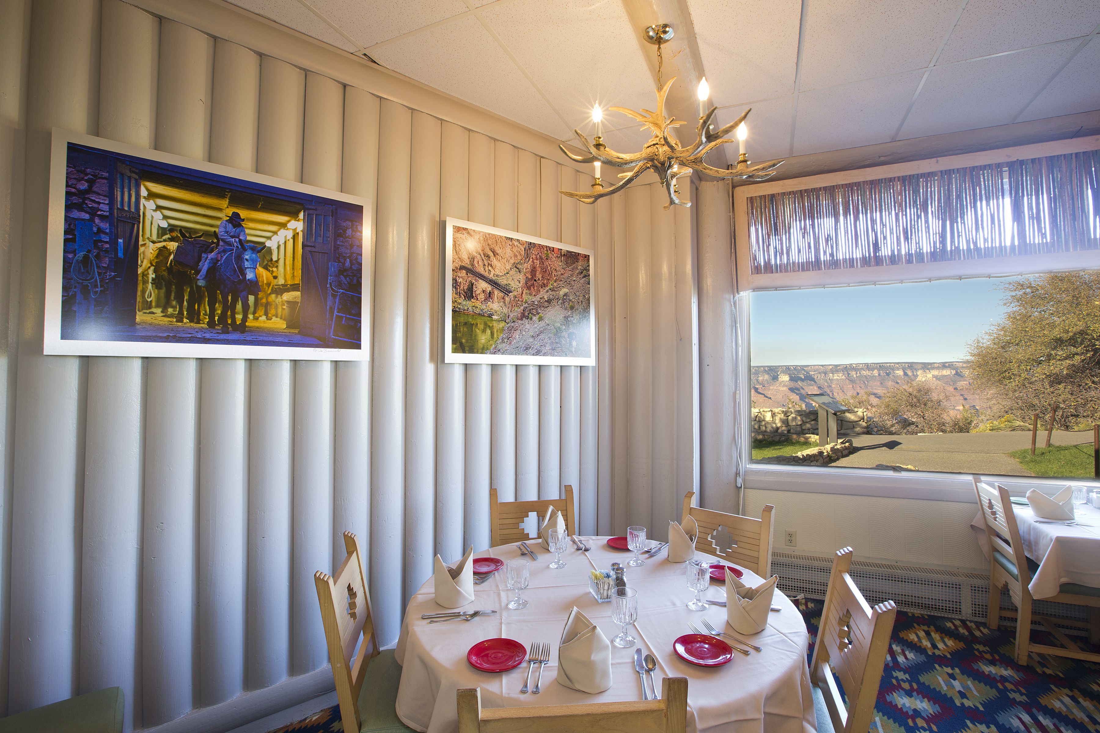 A dining area with a round table set for six, white walls, and a large window with a view of a landscape.