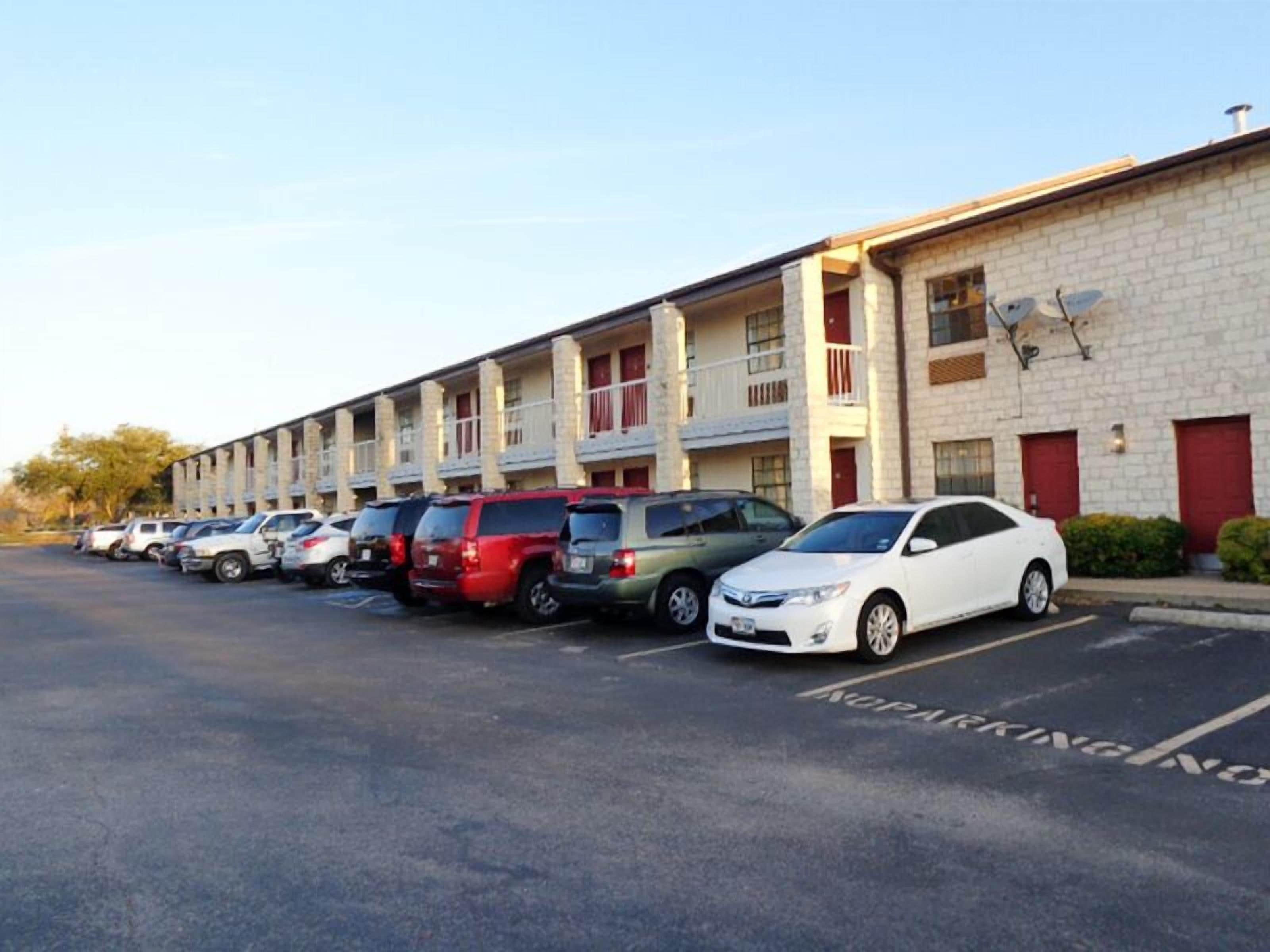 A row of parking spaces in front of a multi-story motel with a brick facade and red doors.