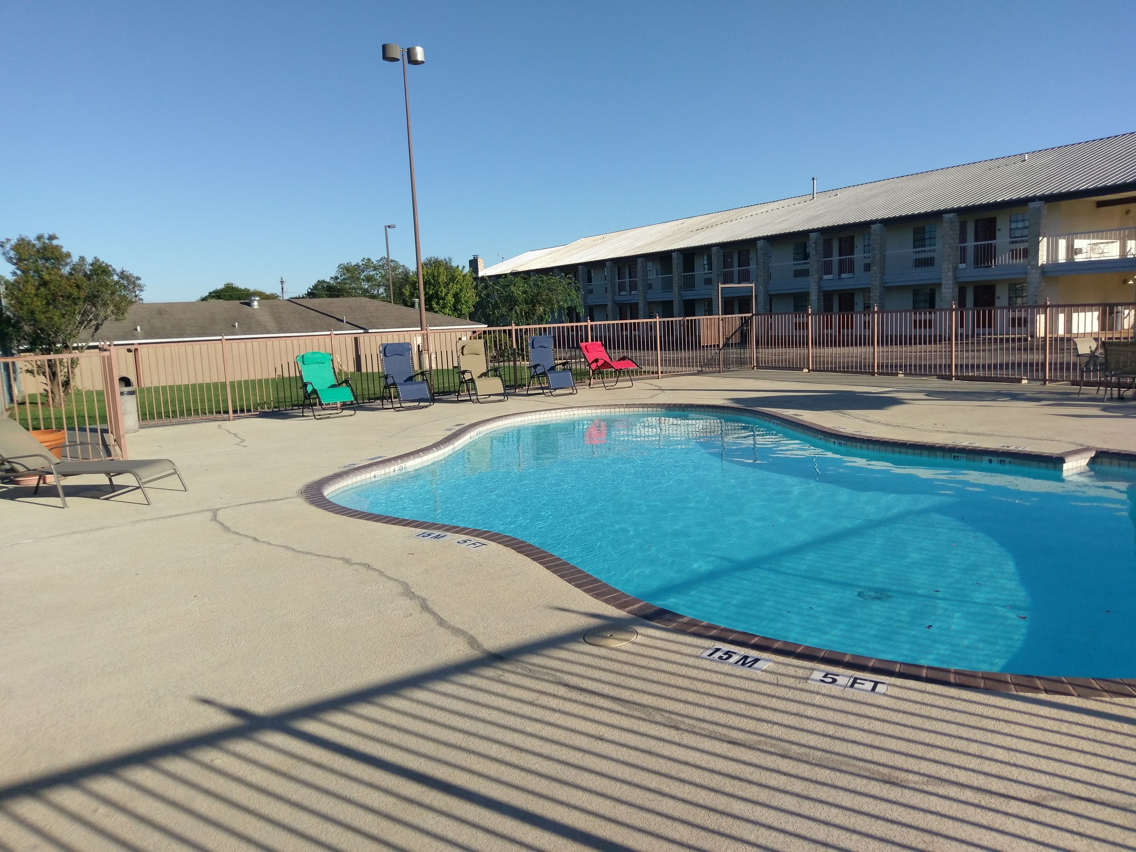 A swimming pool with lounge chairs, a fenced area, and a building with multiple windows and balconies.
