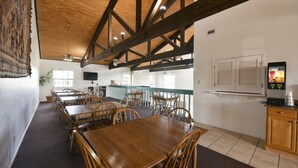 Un restaurante con mesas y sillas de madera, una zona de cocina y un ventanal grande.