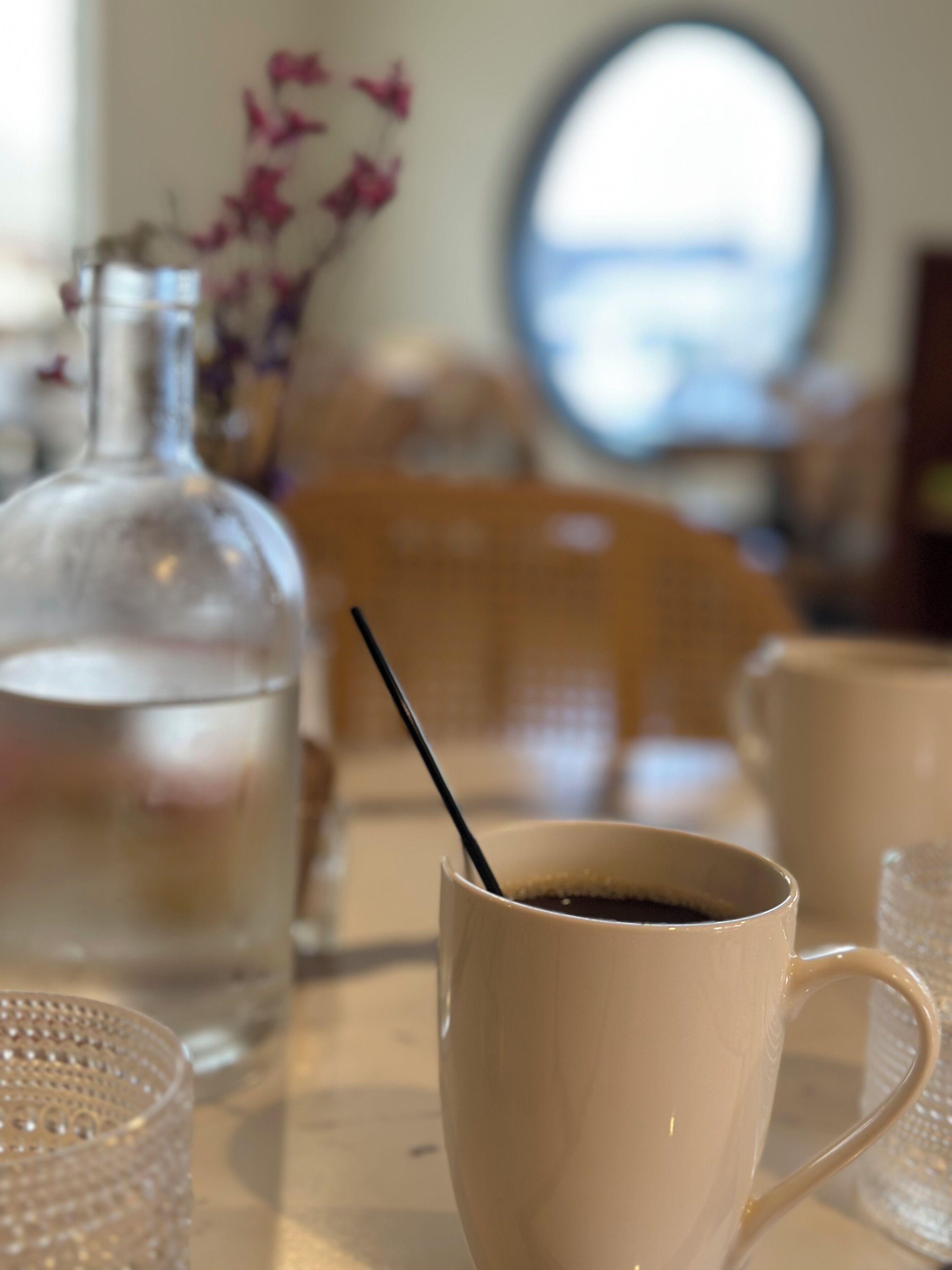 A table with a clear glass bottle, a white mug with a black straw, and a clear glass cup.