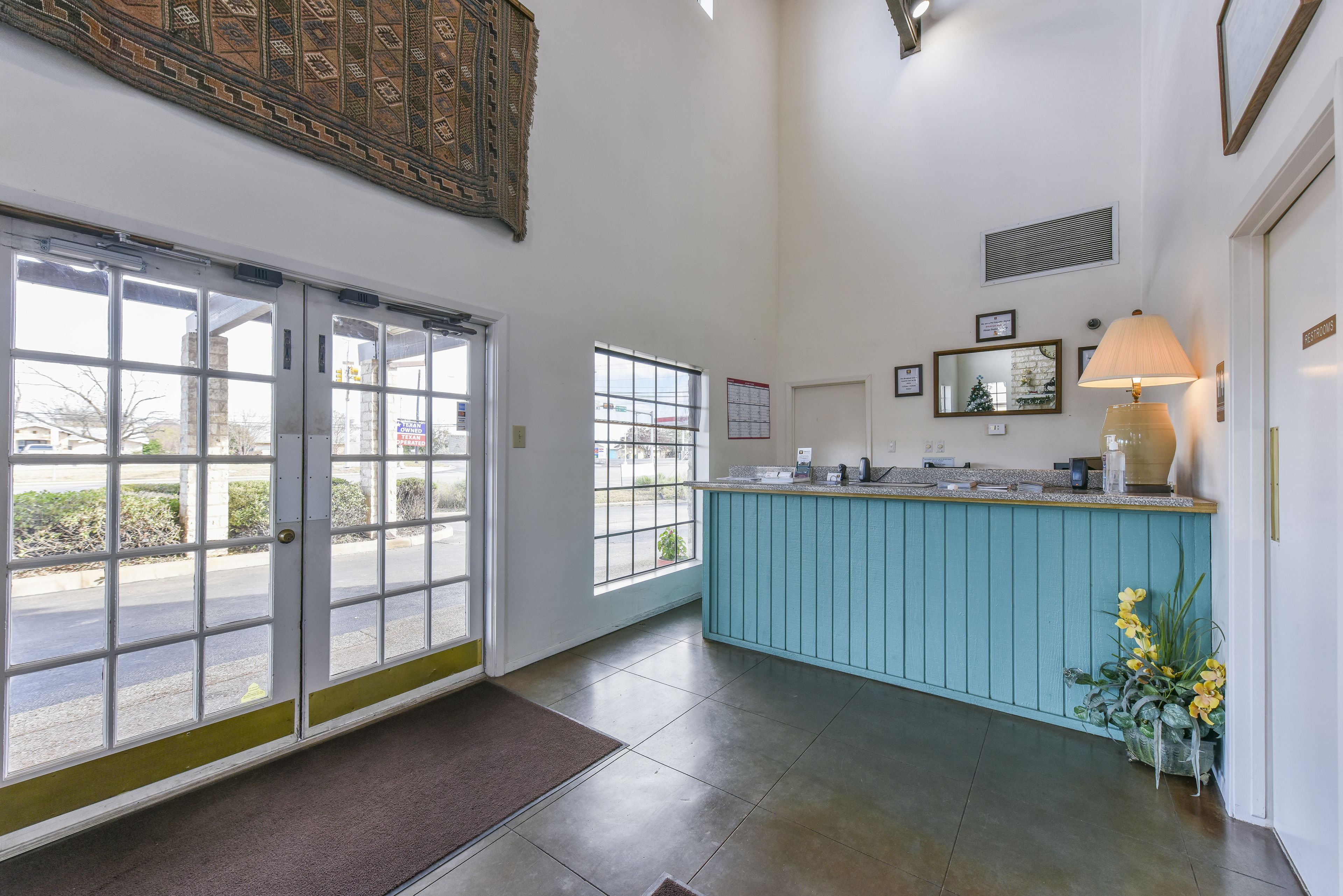 A reception area with a teal counter, large windows, and a door leading outside.