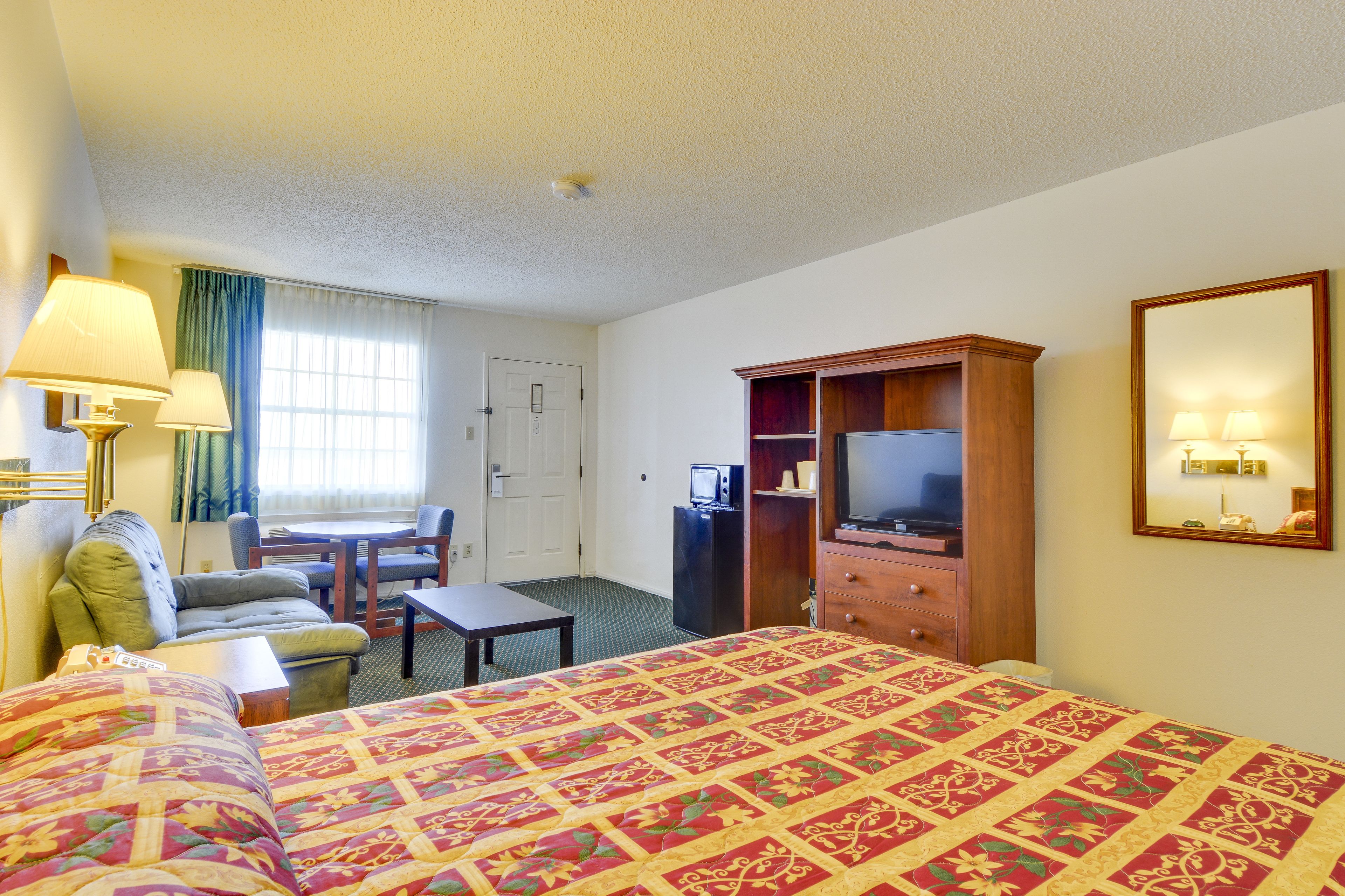 A hotel room with a large bed, a desk with a chair, a television, and a dresser.