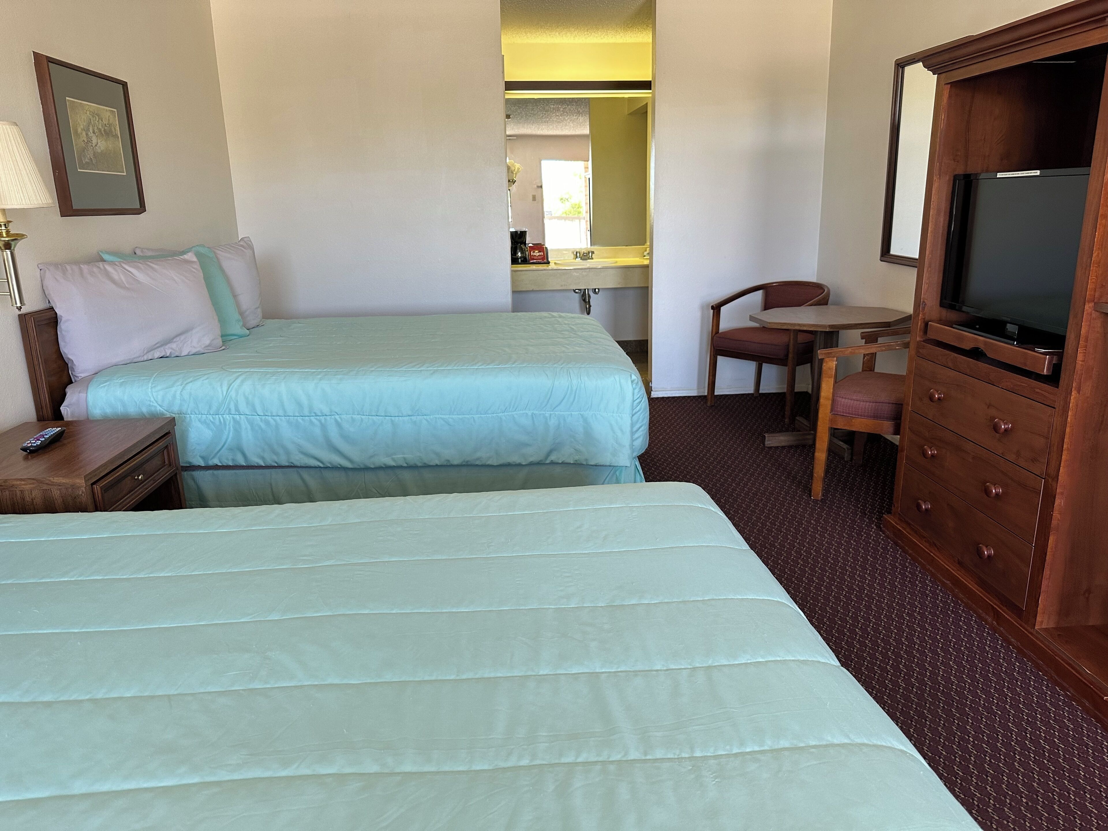 A hotel room with two beds, a desk, a chair, a dresser, a television, and a framed picture on the wall.