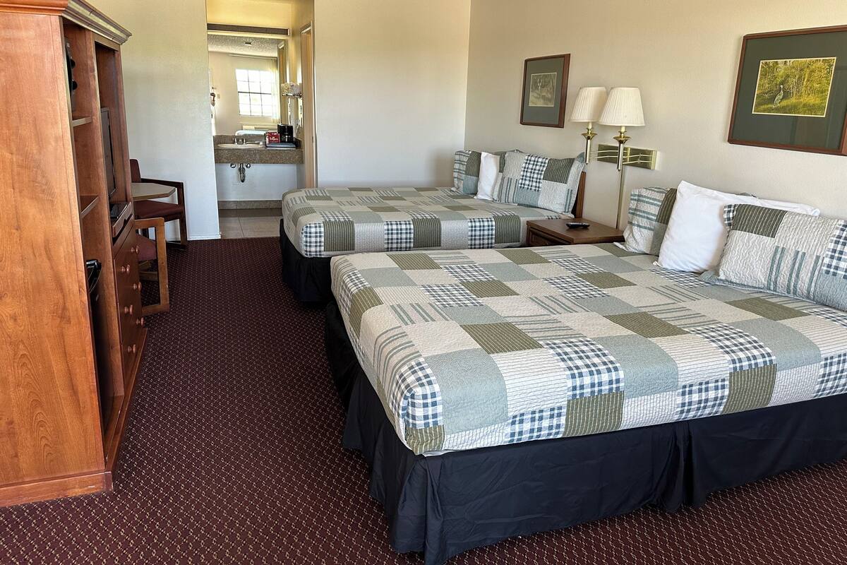 Une chambre d’hôtel avec deux lits, un bureau, une chaise, une armoire, une salle de bain et une fenêtre.