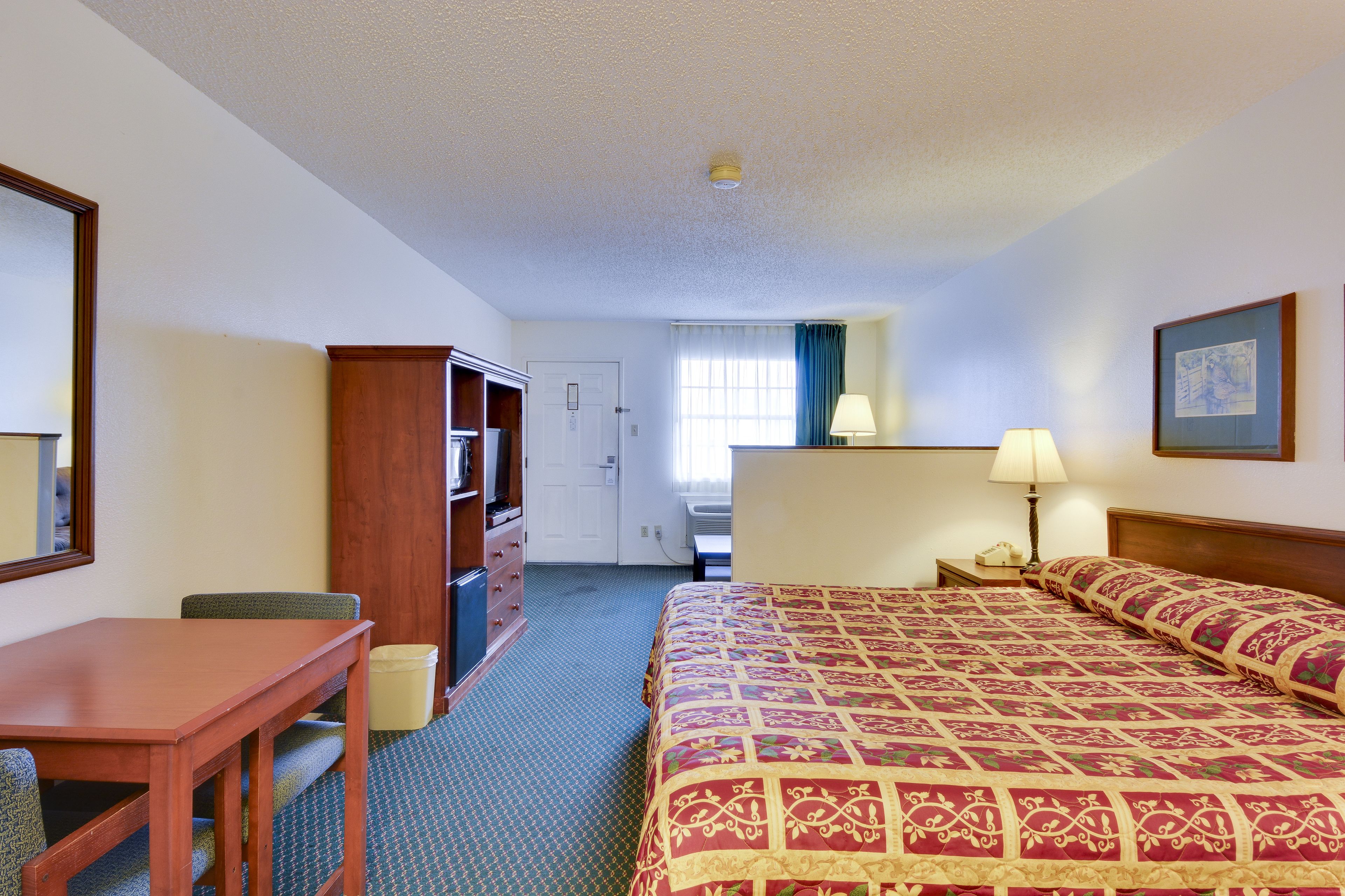 Une chambre d’hôtel avec un lit, un bureau, une chaise, une armoire et une porte de salle de bain.
