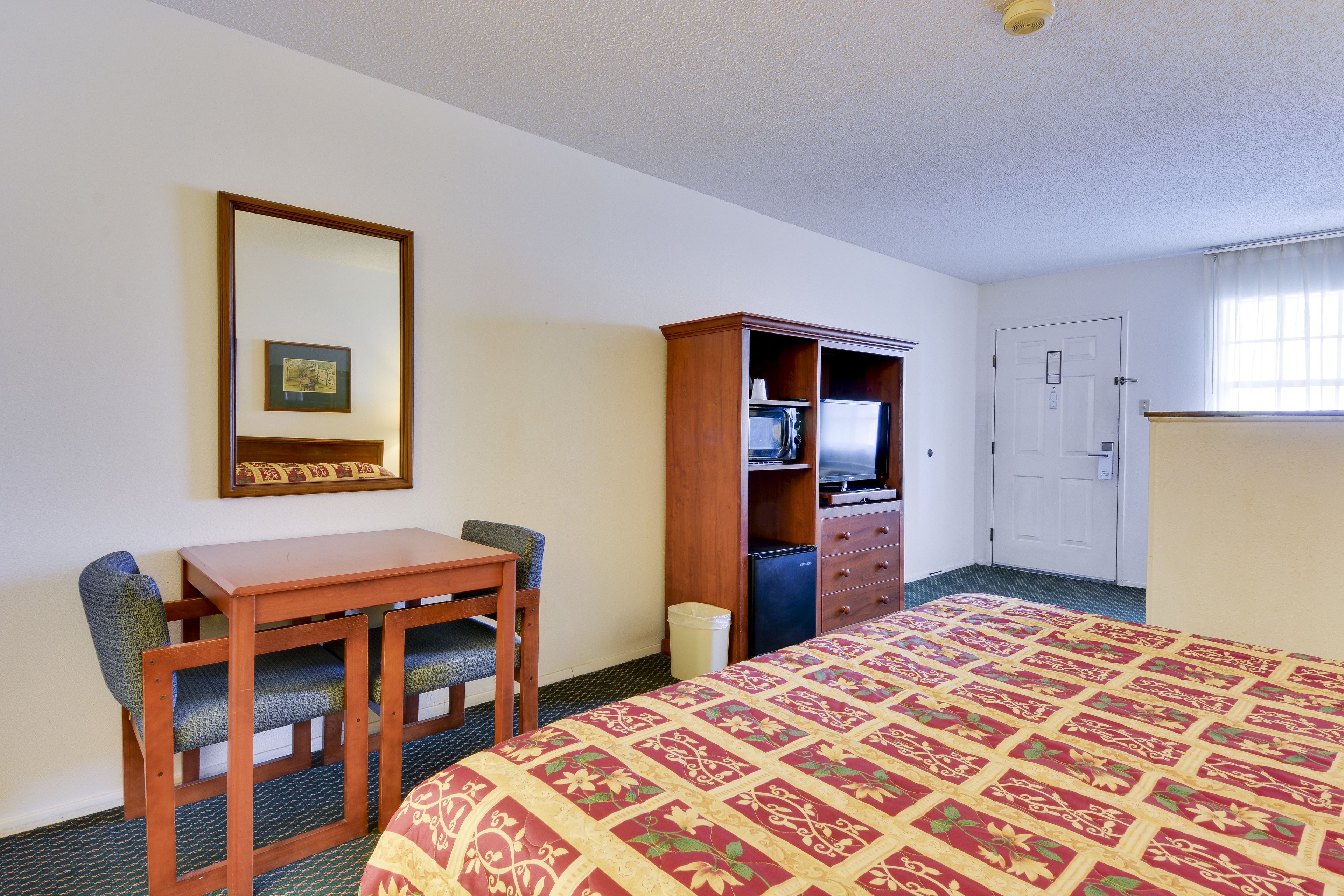 A hotel room with a bed, a desk with two chairs, a wardrobe, a television, and a door.
