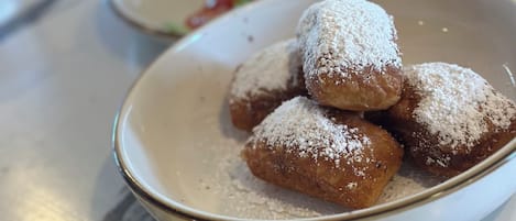 A plate of powdered doughnuts, a burger with a bun, and scrambled eggs on a table.
