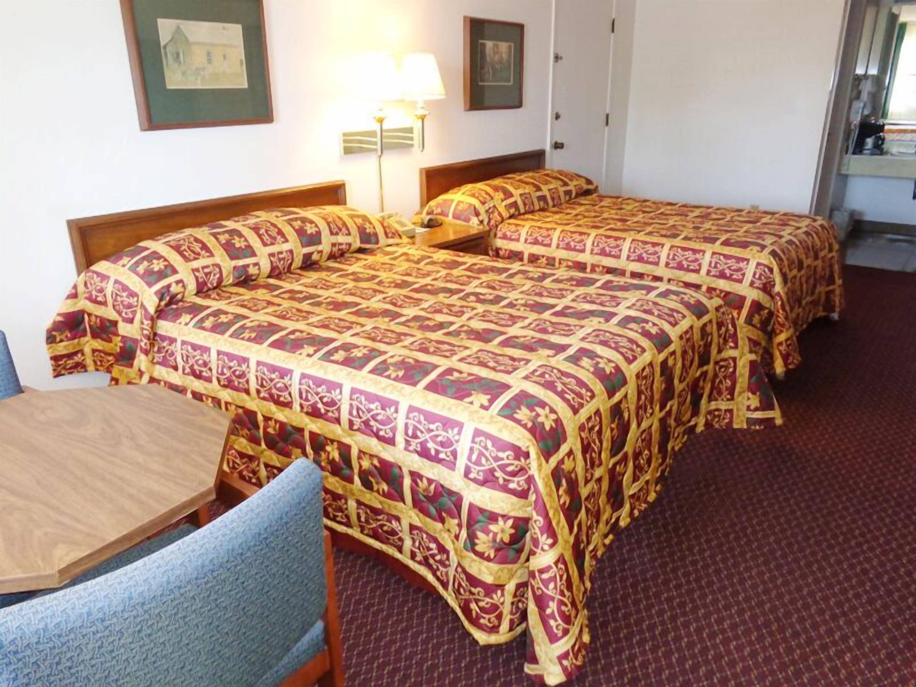 Habitación de hotel con dos camas, una mesa de madera y una silla.