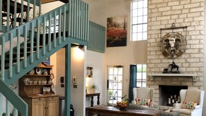 Un salón espacioso con una escalera de madera, una chimenea y un ventanal grande.