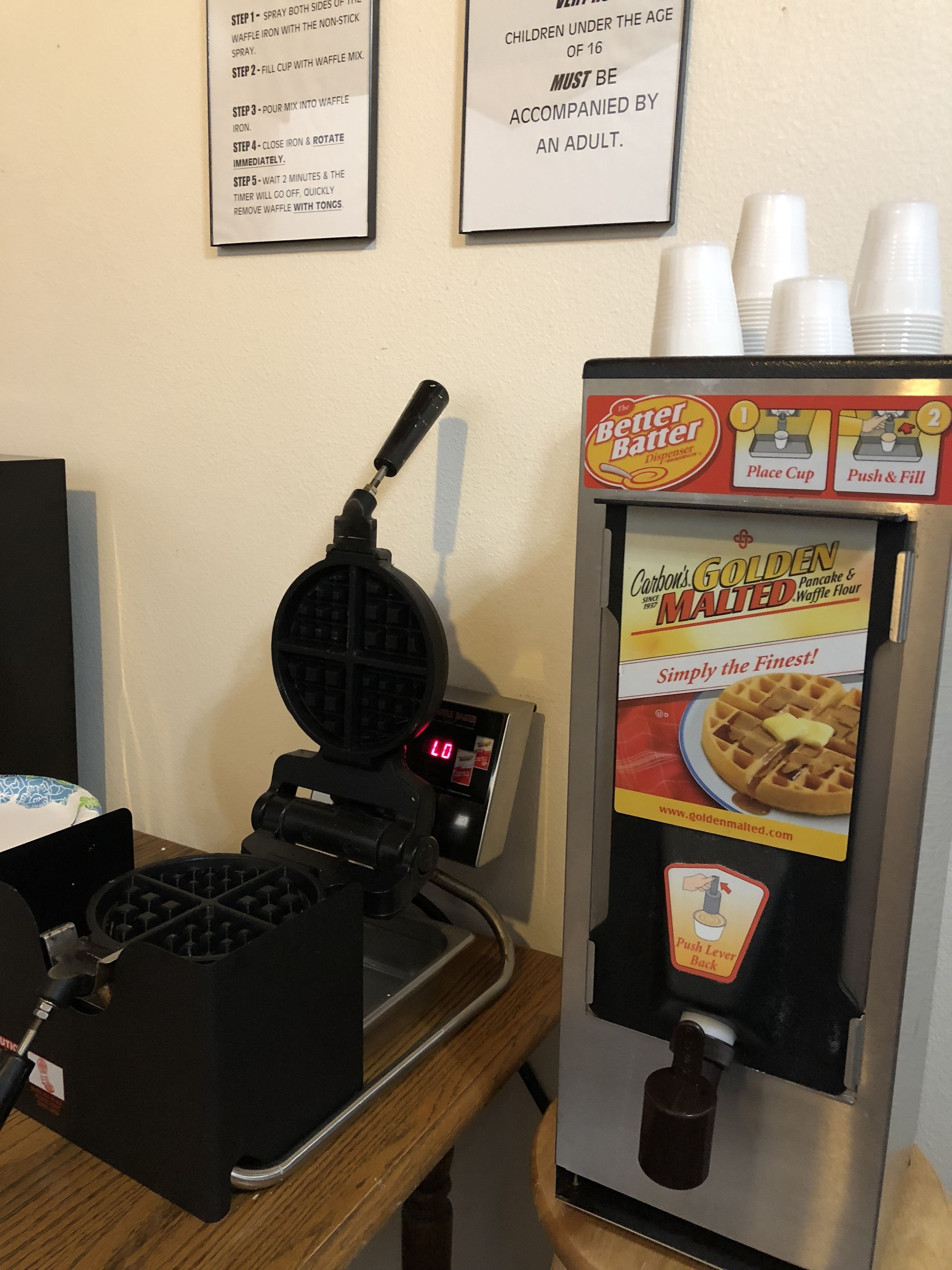 Una plancha para gofres y un dispensador de masa, con instrucciones y un letrero de advertencia.