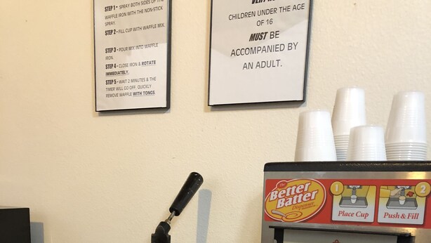 A waffle iron and a batter dispenser with instructions and a warning sign. - Windcrest Inn and Suites (Fredericksburg)