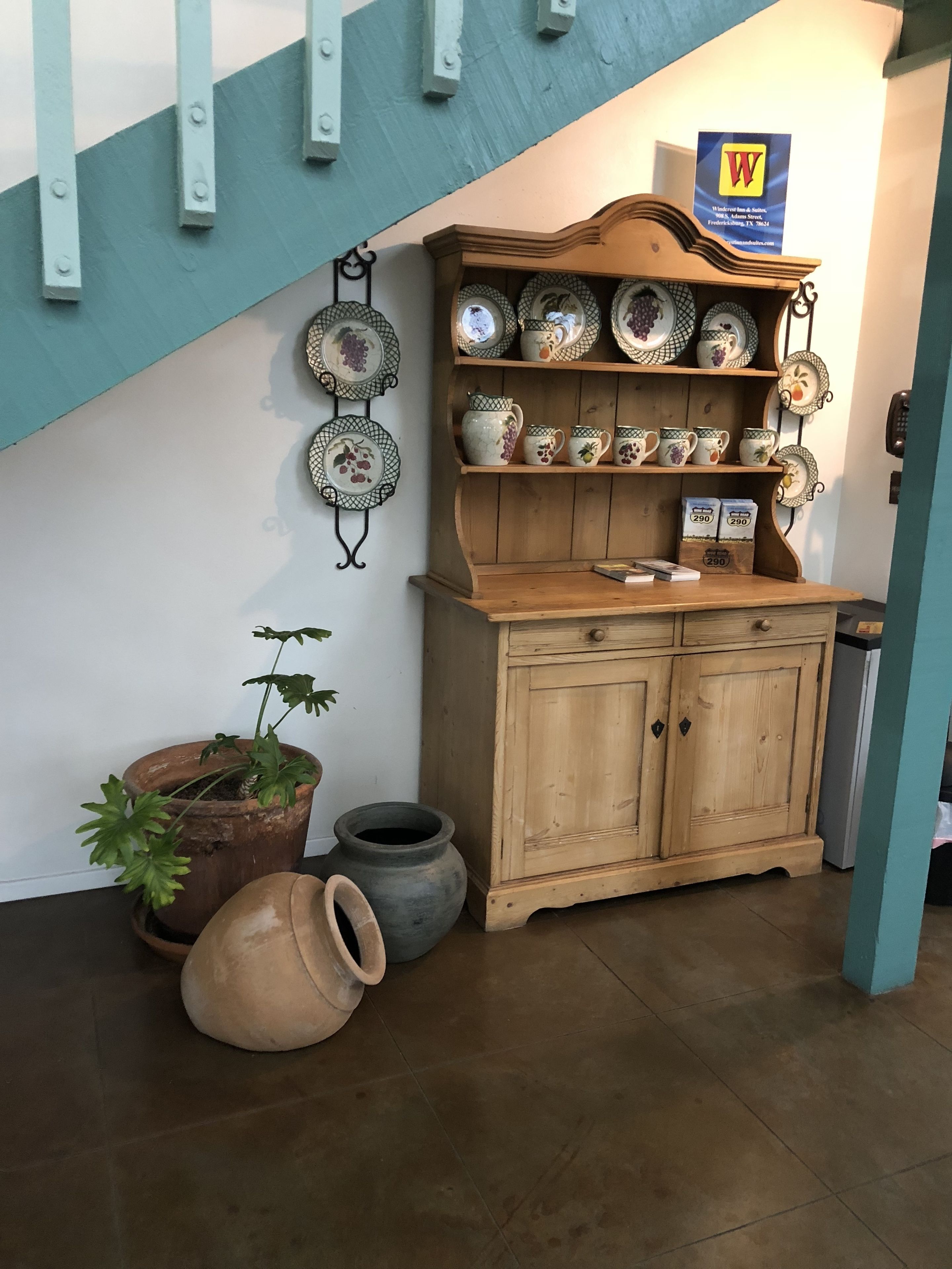 Ein Küchenbereich mit einem Holzschrank, der verschiedene Keramikteller präsentiert, einem hängenden Tellergestell und einem Blumentopf.