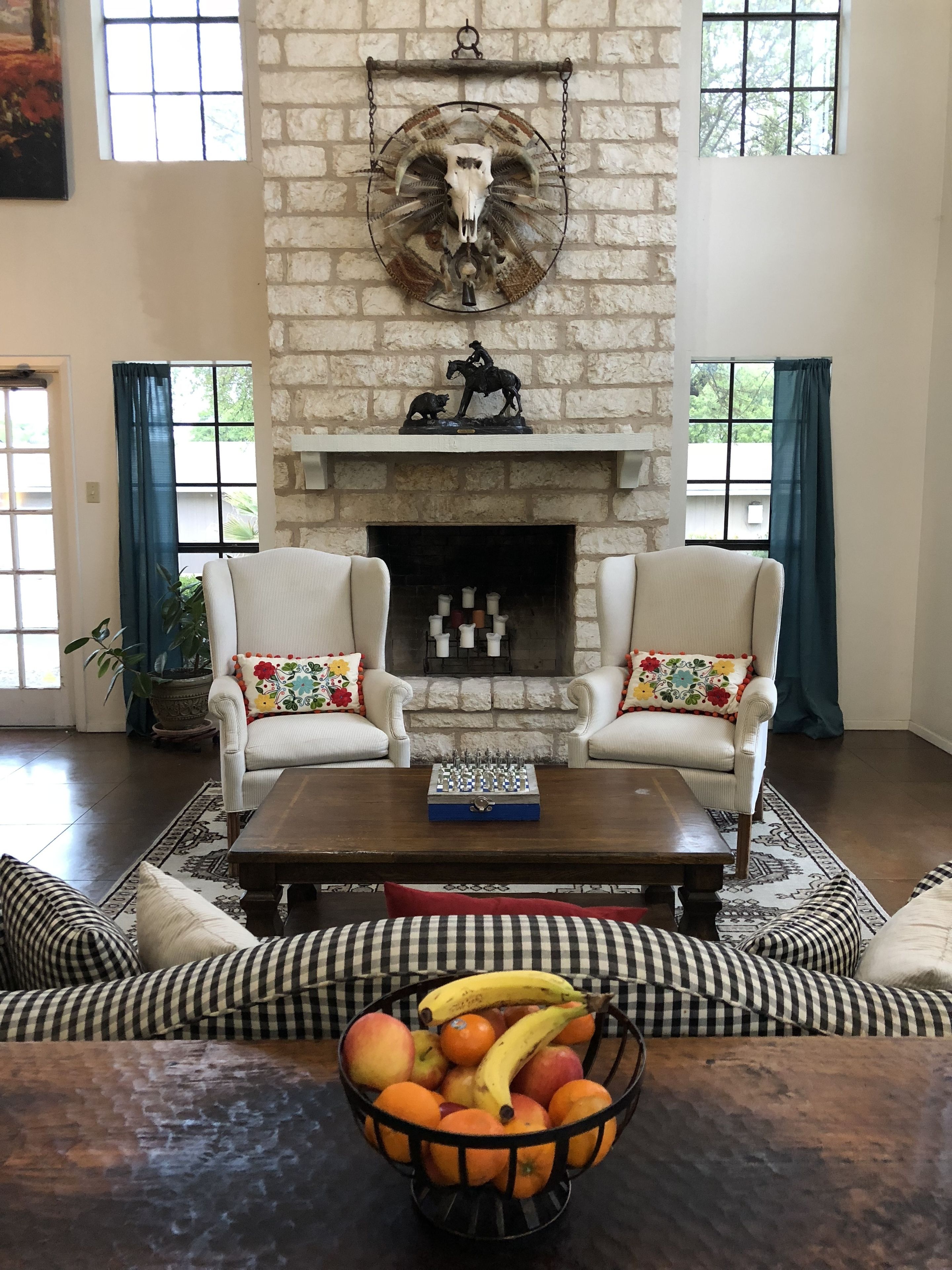 Una sala de estar con dos sillones blancos, una mesa de centro, una chimenea con una escultura montada y un frutero sobre la mesa de centro.