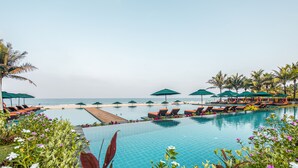 Área da piscina com espreguiçadeiras e guarda-sóis, um deck de madeira e vista para o oceano.