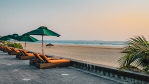 Uma área de estar à beira-mar com fileiras de espreguiçadeiras e guarda-sóis verdes.