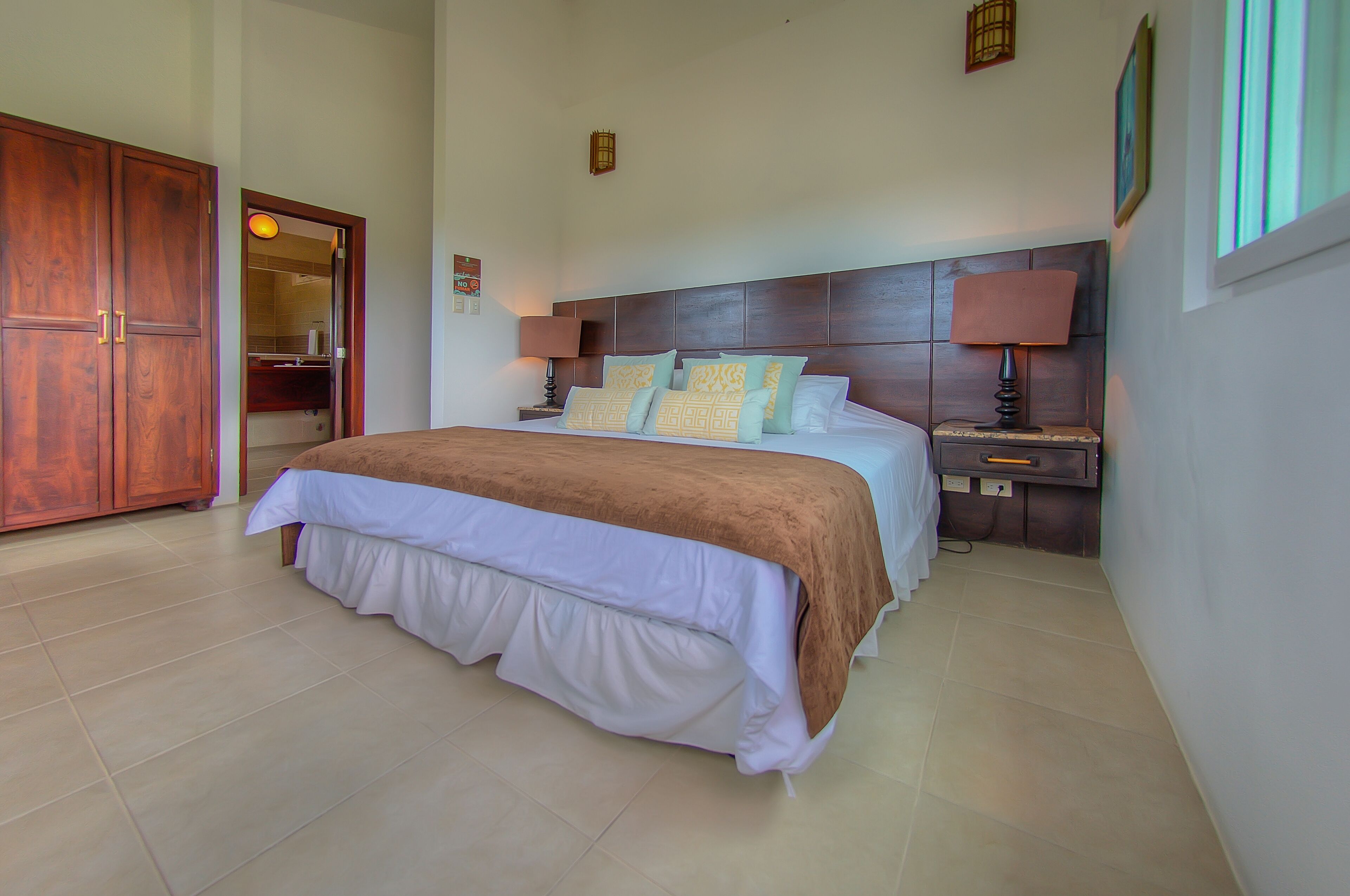 A bedroom with a large bed, wooden wardrobe, bedside tables with lamps, and a mirror.
