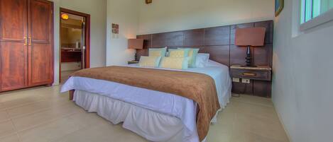 A bedroom with a large bed, wooden wardrobe, bedside tables with lamps, and a mirror.