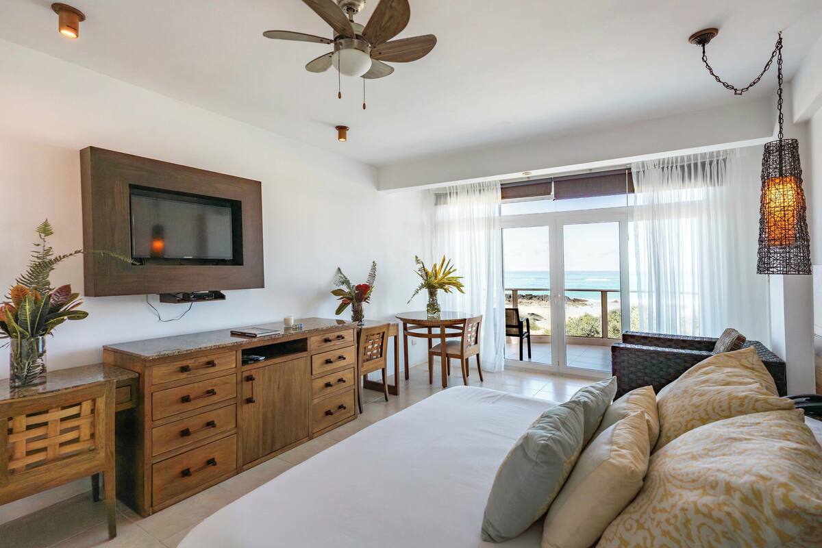 A bedroom with a bed, wooden desk, TV, and a balcony with a view.