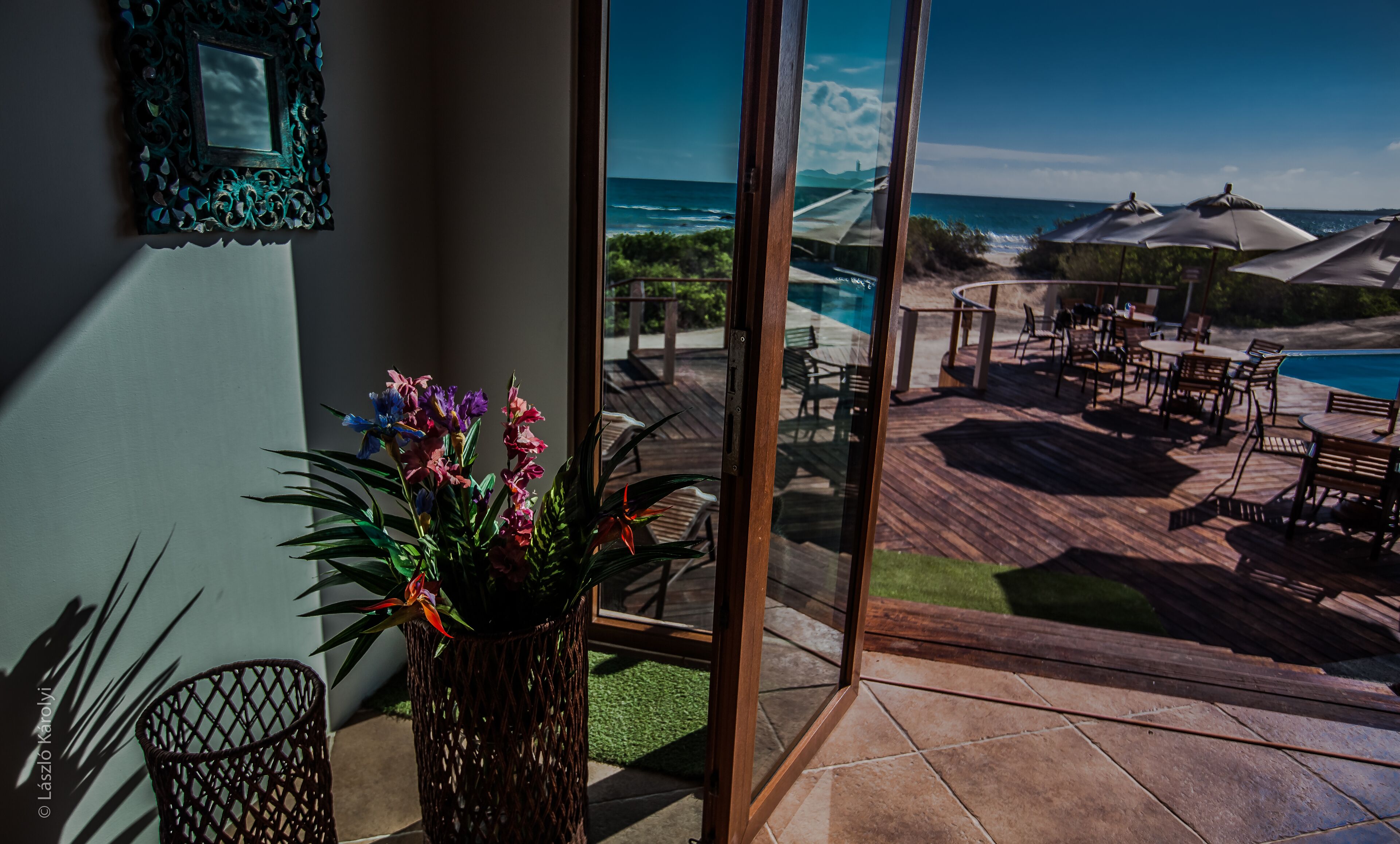 A view from a balcony overlooking a pool area with outdoor furniture and a clear view of the ocean.