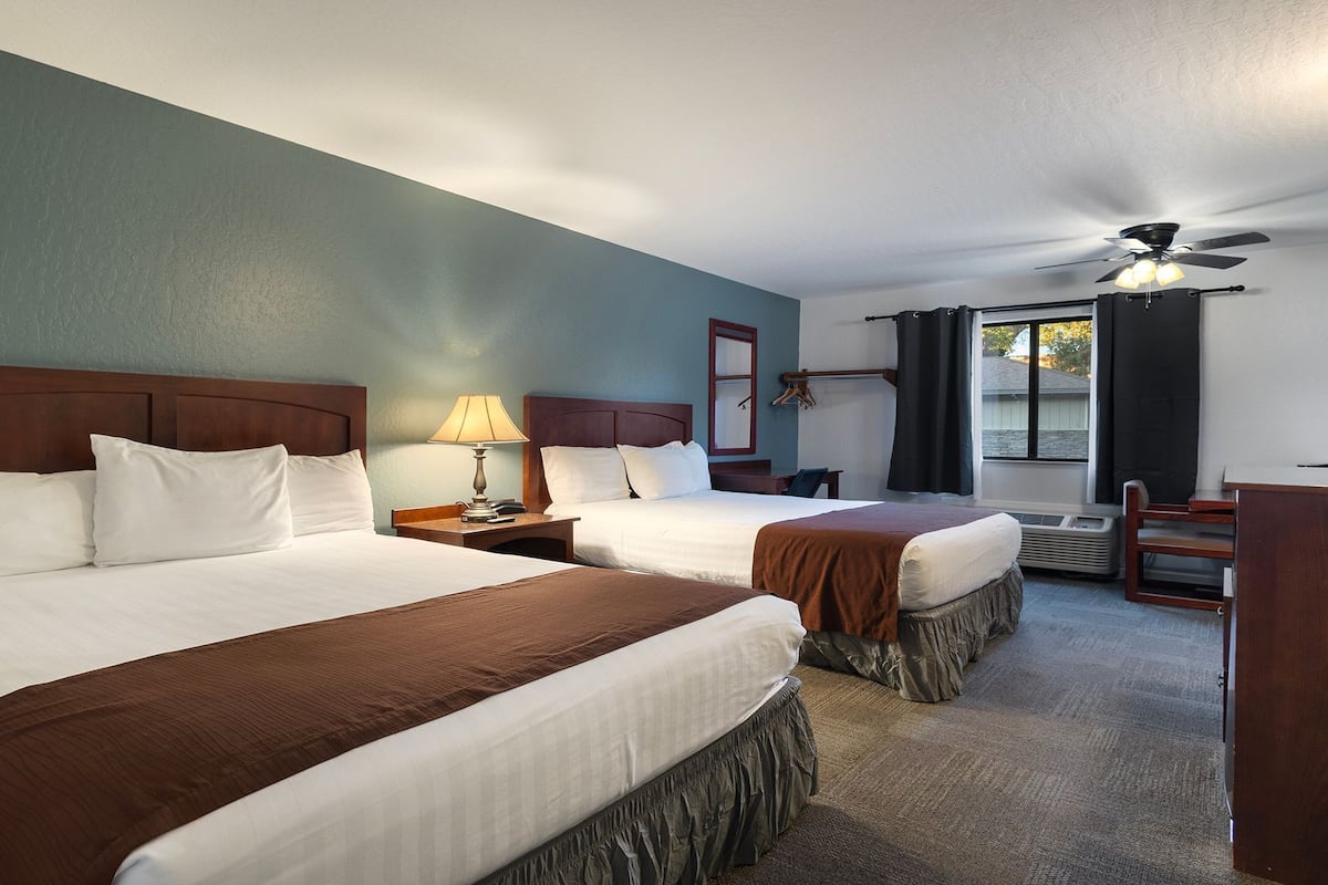 A hotel room with two beds, a desk, a chair, a ceiling fan, and a window with curtains.